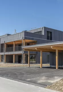 Mehrfamilienhaus Truberholzhaus Recherswil, Schweizer Holz, Truberholzwände sind nicht sichtbar, die Dübel sind nicht sichtbar, Fassade ist vorvergraut, es hat eine Attikawohnung, im Erdgeschoss und Obergeschoss hat es Loggaeinschnitte (Terrasse, Balkon), moderner Neubau, auf dem Dach ist ein Sonnensegel, Flachdach mit Solarpanel, es hat kein Keller dafür ein zusätzliches Gebäude mit Autounterstand und Lagerraum, Umschwung mit Rasen 