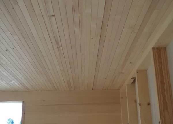 Decke und Wand aus hellen Holzpaneelen in einem Neubau, sorgfältig verarbeitet mit sichtbarer Maserung und klaren Linien.
