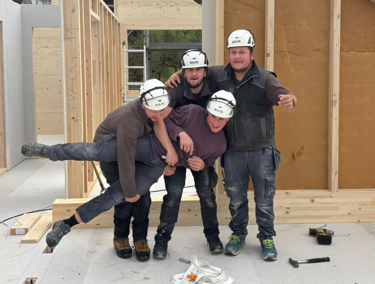 Vier Zimmerleute posieren lachend auf der Baustelle eines Holzhauses. Die fröhliche Stimmung zeigt den Teamgeist und die Freude am Handwerk bei der Zimmerei Hirschi AG.