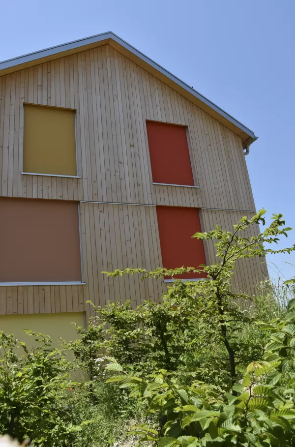 Mehrfamilienhaus in Lyss. Das Haus ist von einem Naturgarten umschlungen. Die Storen sind nach einem Farbmuster von der Bauherrin ausgewählt.