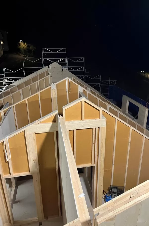 Baustelle eines Holzbaus bei Sonnenuntergang. Die beleuchtete Holzkonstruktion und das eingerüstete Gebäude zeigen den fortgeschrittenen Aufbau eines modernen Holzhauses durch die Zimmerei Hirschi AG.