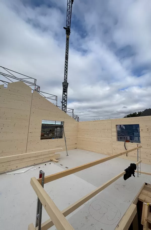 Baustelle eines Holzbaus bei Sonnenuntergang. Die beleuchtete Holzkonstruktion und das eingerüstete Gebäude zeigen den fortgeschrittenen Aufbau eines modernen Holzhauses durch die Zimmerei Hirschi AG.