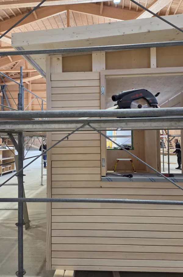 Blick in die Produktionshalle der Zimmerei Hirschi: Ein vorgefertigtes Holzmodul steht im Zentrum der Werkstatt, umgeben von Maschinen, Werkbänken und Holzbauelementen. Die industrielle Vorfertigung zeigt präzise Holzbauarbeit unter kontrollierten Bedingungen.