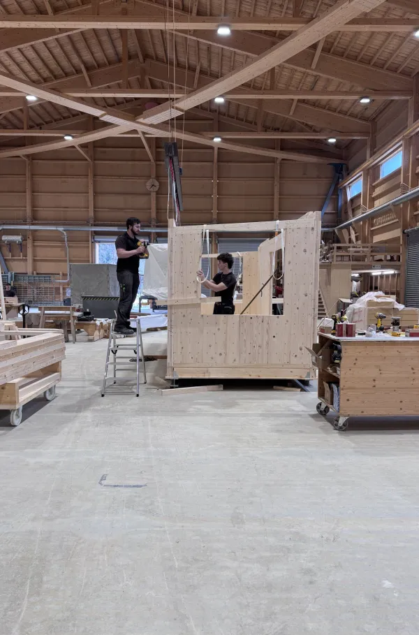 Blick in die Produktionshalle der Zimmerei Hirschi: Ein vorgefertigtes Holzmodul steht im Zentrum der Werkstatt, umgeben von Maschinen, Werkbänken und Holzbauelementen. Die industrielle Vorfertigung zeigt präzise Holzbauarbeit unter kontrollierten Bedingungen.
