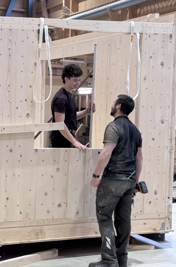 Blick in die Produktionshalle der Zimmerei Hirschi: Ein vorgefertigtes Holzmodul steht im Zentrum der Werkstatt, umgeben von Maschinen, Werkbänken und Holzbauelementen. Die industrielle Vorfertigung zeigt präzise Holzbauarbeit unter kontrollierten Bedingungen.