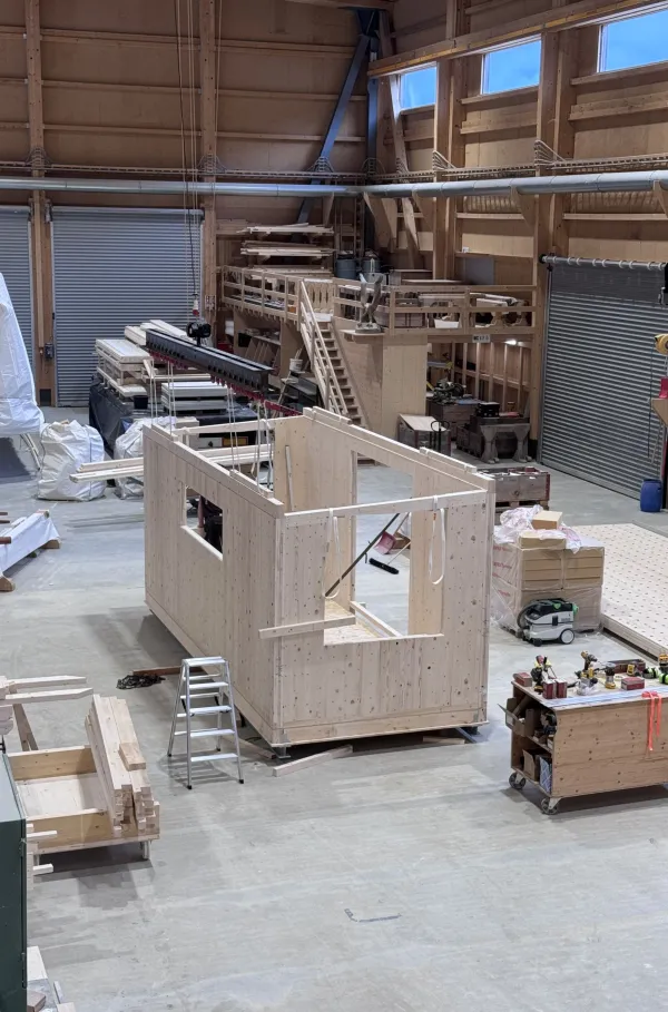 Blick in die Produktionshalle der Zimmerei Hirschi: Ein vorgefertigtes Holzmodul steht im Zentrum der Werkstatt, umgeben von Maschinen, Werkbänken und Holzbauelementen. Die industrielle Vorfertigung zeigt präzise Holzbauarbeit unter kontrollierten Bedingungen.
