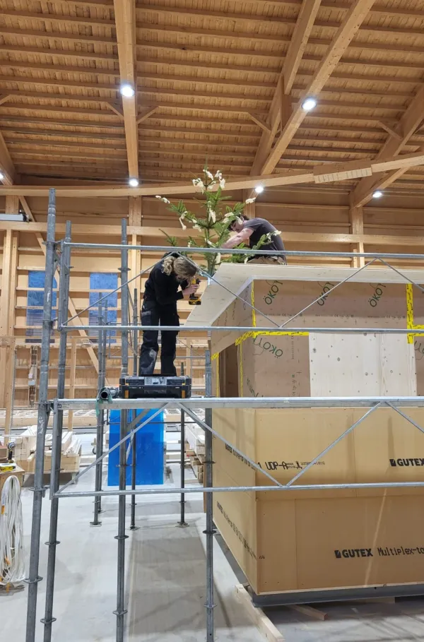 Blick in die Produktionshalle der Zimmerei Hirschi: Ein vorgefertigtes Holzmodul steht im Zentrum der Werkstatt, umgeben von Maschinen, Werkbänken und Holzbauelementen. Die industrielle Vorfertigung zeigt präzise Holzbauarbeit unter kontrollierten Bedingungen.