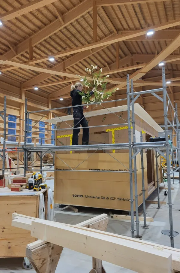 Blick in die Produktionshalle der Zimmerei Hirschi: Ein vorgefertigtes Holzmodul steht im Zentrum der Werkstatt, umgeben von Maschinen, Werkbänken und Holzbauelementen. Die industrielle Vorfertigung zeigt präzise Holzbauarbeit unter kontrollierten Bedingungen.