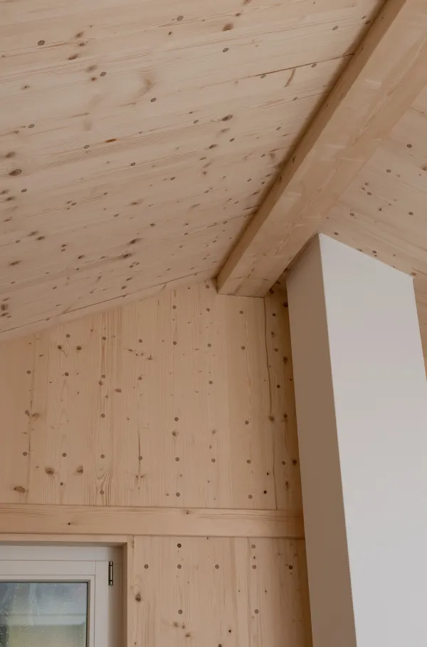 Modernes Badezimmer mit grossformatigen grauen Fliesen, Badewanne und Waschtisch mit hölzernem Unterschrank. Die helle, geneigte Holzdecke und die sichtbaren Holzelemente schaffen einen warmen Kontrast zur schlichten Badezimmereinrichtung.