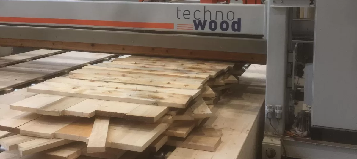 In unserer Produktionsstätte in Trub haben die Arbeiten zu den Wandelementen begonnen. Die Fertigungsanlage umfasst einen Produktionstisch, ein Dübelportal und ein Abbundportal. Die auf dem Produktionstisch ausgelegten Bretter werden vom Dübelportal vollautomatisch bei den Kreuzungspunkten verbunden. Das Abbundportal fräst die Konturen, bohrt die Steckdosen, kehlt die Verbindungsnuten und kalibriert die Elemente auf die gewünschte Dicke.