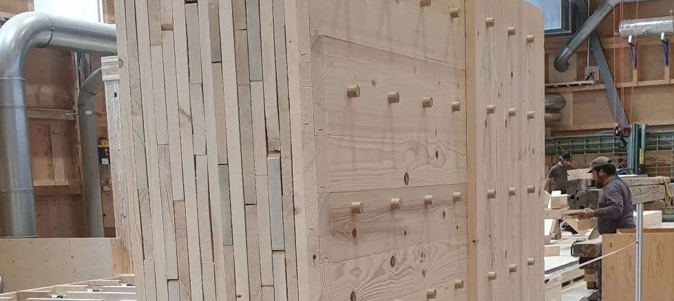 In unserer Produktionsstätte in Trub haben die Arbeiten zu den Wandelementen begonnen. Die Fertigungsanlage umfasst einen Produktionstisch, ein Dübelportal und ein Abbundportal. Die auf dem Produktionstisch ausgelegten Bretter werden vom Dübelportal vollautomatisch bei den Kreuzungspunkten verbunden. Das Abbundportal fräst die Konturen, bohrt die Steckdosen, kehlt die Verbindungsnuten und kalibriert die Elemente auf die gewünschte Dicke.