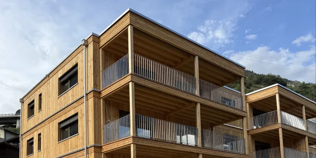 Mehrfamilienhaus in moderner Holzbauweise mit vier Geschossen, grosszügigen Balkonen und Holzfassade.
