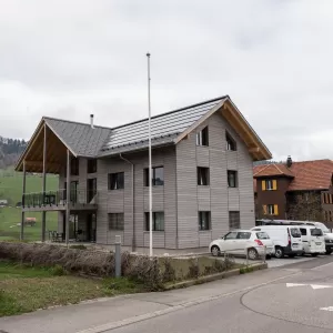 Truberholz Mehrfamilienhaus. Aussenschalung vor vergrautes Falzbrett aus Tanne, integrierte Sauna in Ferienwohnung, Saunawand aus Tanne, Möbel in der Saune aus Arven Holz, Truberholz-Wände innen sichtbar, inklusive Decke Dachschräge, Gebäudehülle Truberholz sichtbar, Innendecke Brettstapel, Boden ist alles Trockenbauaufbau, Zimmer und Bad aus Tannen Holz und allgemein Räume sind Buchenriemenboden. Türen sind alle Massivholz mit Blockfutter aus Tanne.
