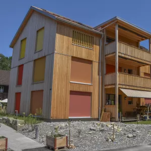 Mehrfamilienhaus in Lyss. Das Haus ist von einem Naturgarten umschlungen. Die Storen sind nach einem Farbmuster von der Bauherrin ausgewählt.