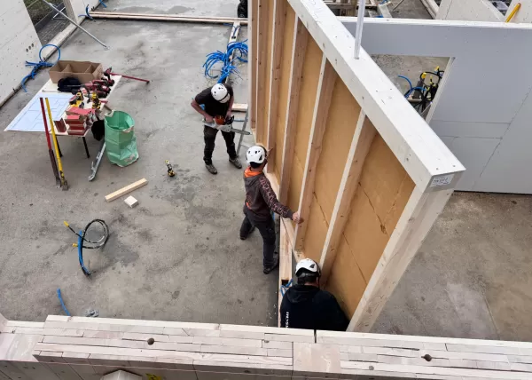 Baustelle eines Holzbaus bei Sonnenuntergang. Die beleuchtete Holzkonstruktion und das eingerüstete Gebäude zeigen den fortgeschrittenen Aufbau eines modernen Holzhauses durch die Zimmerei Hirschi AG.