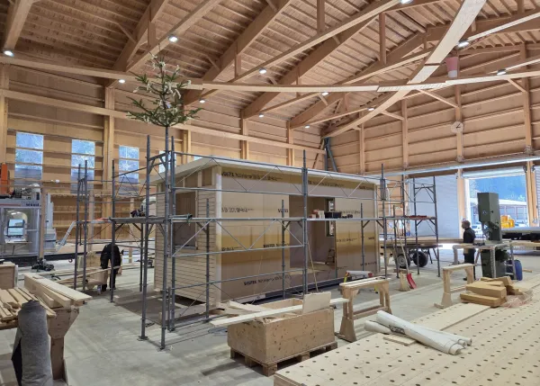 Blick in die Produktionshalle der Zimmerei Hirschi: Ein vorgefertigtes Holzmodul steht im Zentrum der Werkstatt, umgeben von Maschinen, Werkbänken und Holzbauelementen. Die industrielle Vorfertigung zeigt präzise Holzbauarbeit unter kontrollierten Bedingungen.