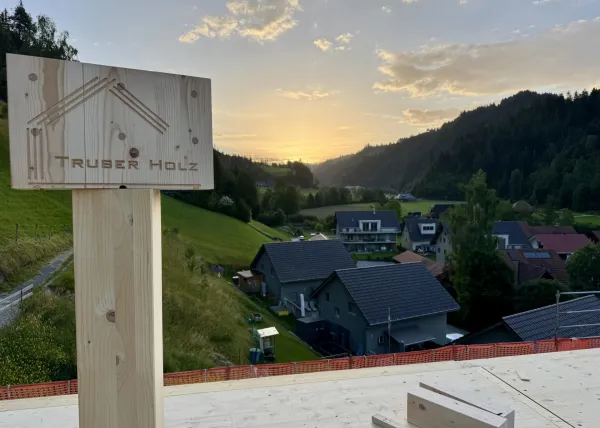 Zimmerleute montieren während der Aufrichtearbeiten eine vorgefertigte Holzkonstruktion auf einem Gebäude. Ein Kran hebt ein grosses Dachelement an seinen Platz, während mehrere Fachkräfte auf dem Dach die Montage begleiten.